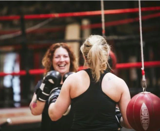 Two Revenge members smiling together during boxing pad work
