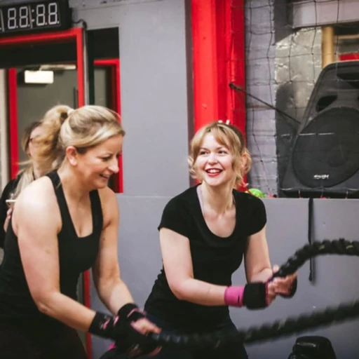 Two women laughing while training with battle ropes